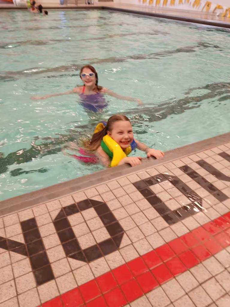Two girls swimming by the side of the pool.